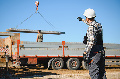 Image of construction worker directing the movement of a crane's sling unloading a lorry